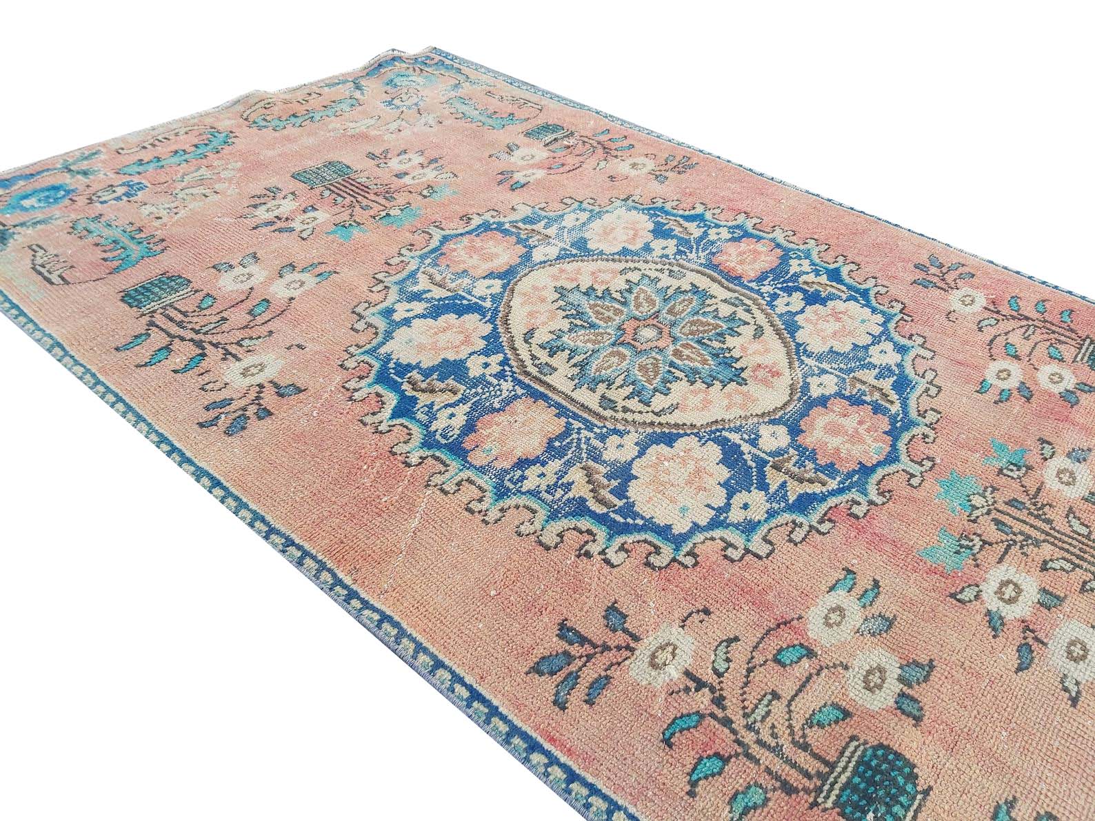 A vintage handmade Turkish wool rug featuring a central blue floral medallion on a pink field.