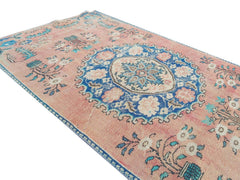 A vintage handmade Turkish wool rug featuring a central blue floral medallion on a pink field.