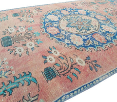 A vintage handmade Turkish wool rug featuring a pink field with blue floral and medallion motifs.