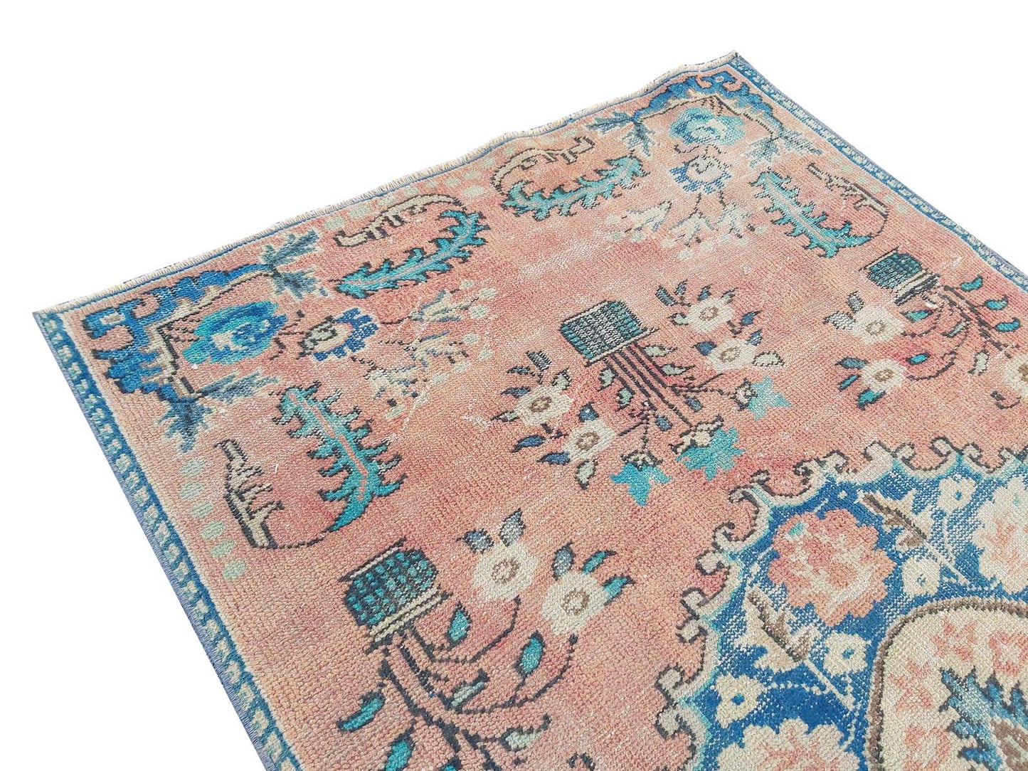 A vintage handmade Turkish rug featuring a faded pink field with blue floral and geometric motifs.