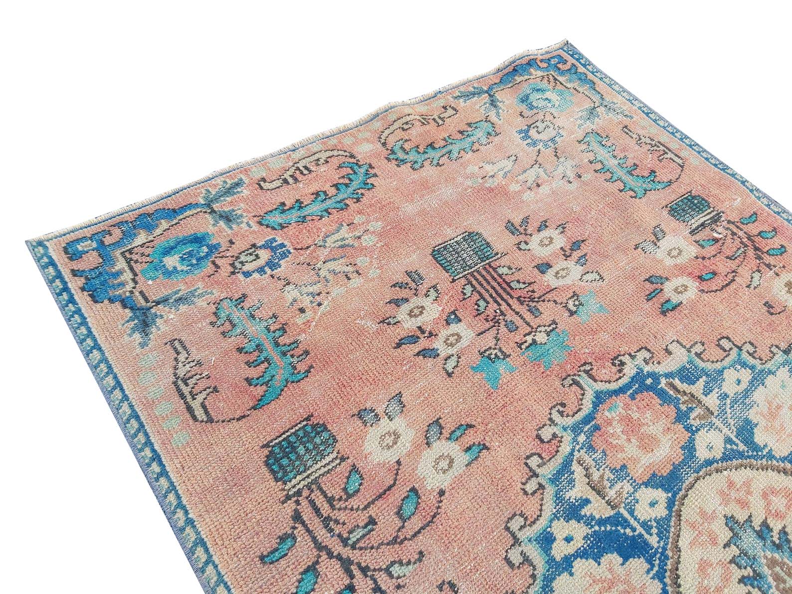 A vintage handmade Turkish rug featuring a faded pink field with blue floral and geometric motifs.