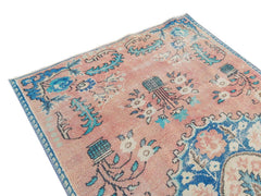 A vintage handmade Turkish rug featuring a faded pink field with blue floral and geometric motifs.