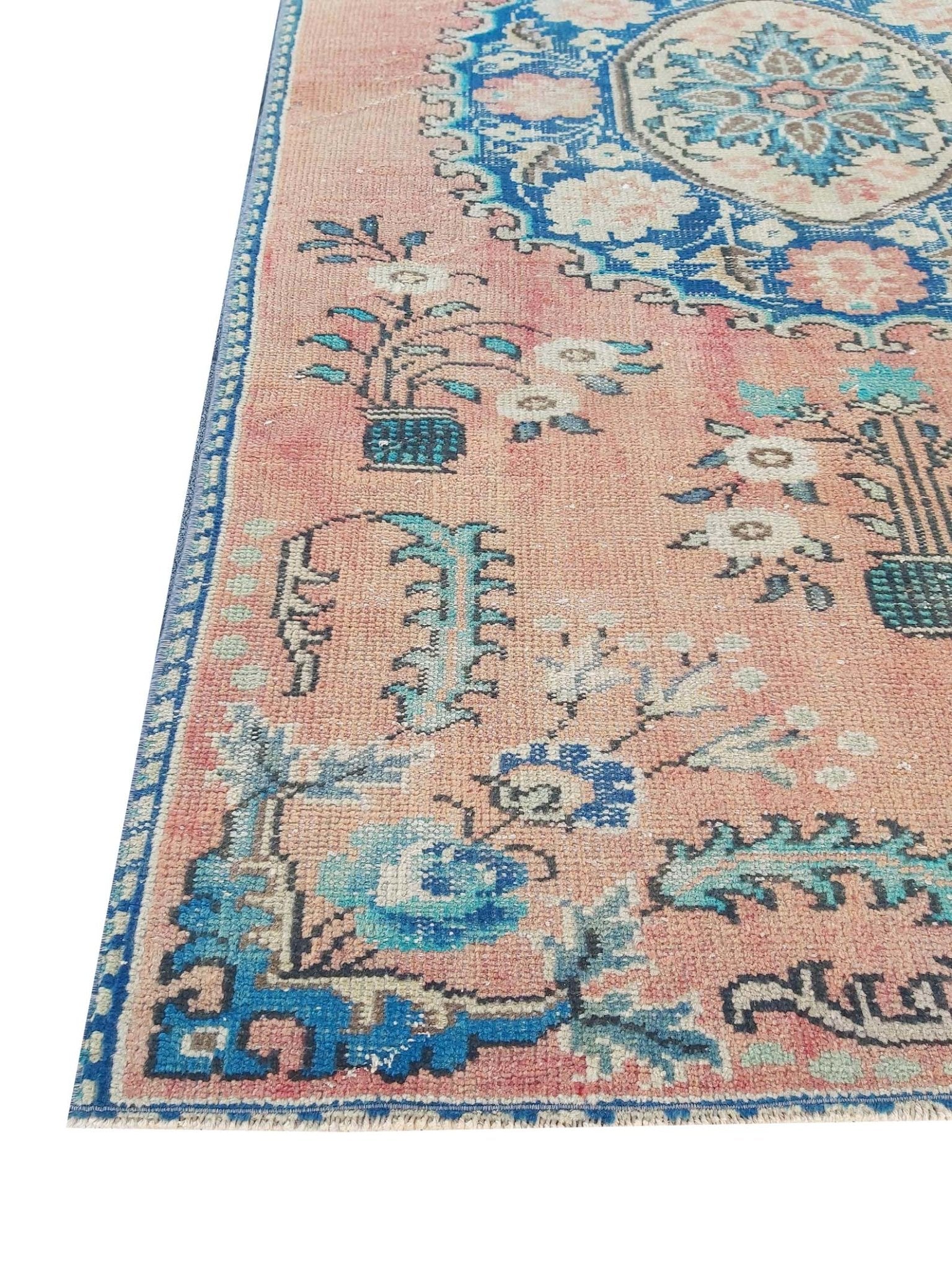 A vintage handmade Turkish wool rug featuring a floral pattern in shades of pink and blue.