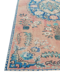 A vintage handmade Turkish wool rug featuring a floral pattern in shades of pink and blue.