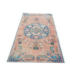 A vintage handmade Turkish wool rug featuring a central blue floral medallion on a pink field.
