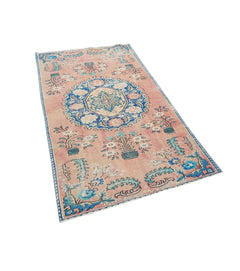 A vintage handmade Turkish wool rug featuring a floral medallion pattern in pink and blue tones.