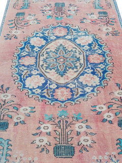 A vintage Turkish rug featuring a central blue floral medallion on a faded pink background.