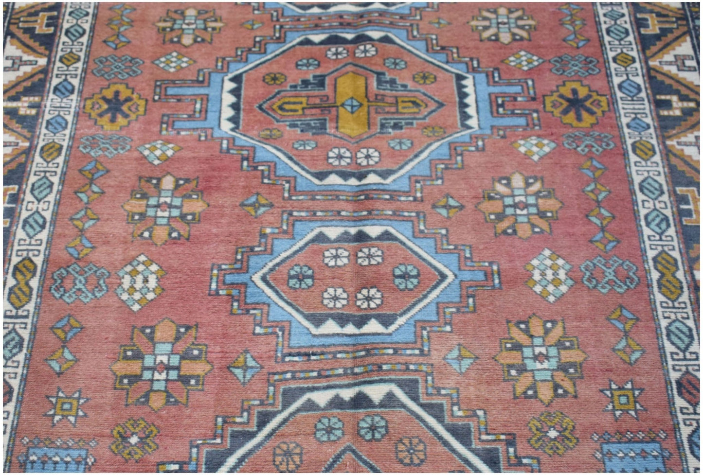 A vintage handwoven Turkish wool rug featuring geometric medallions in red, blue, and yellow.