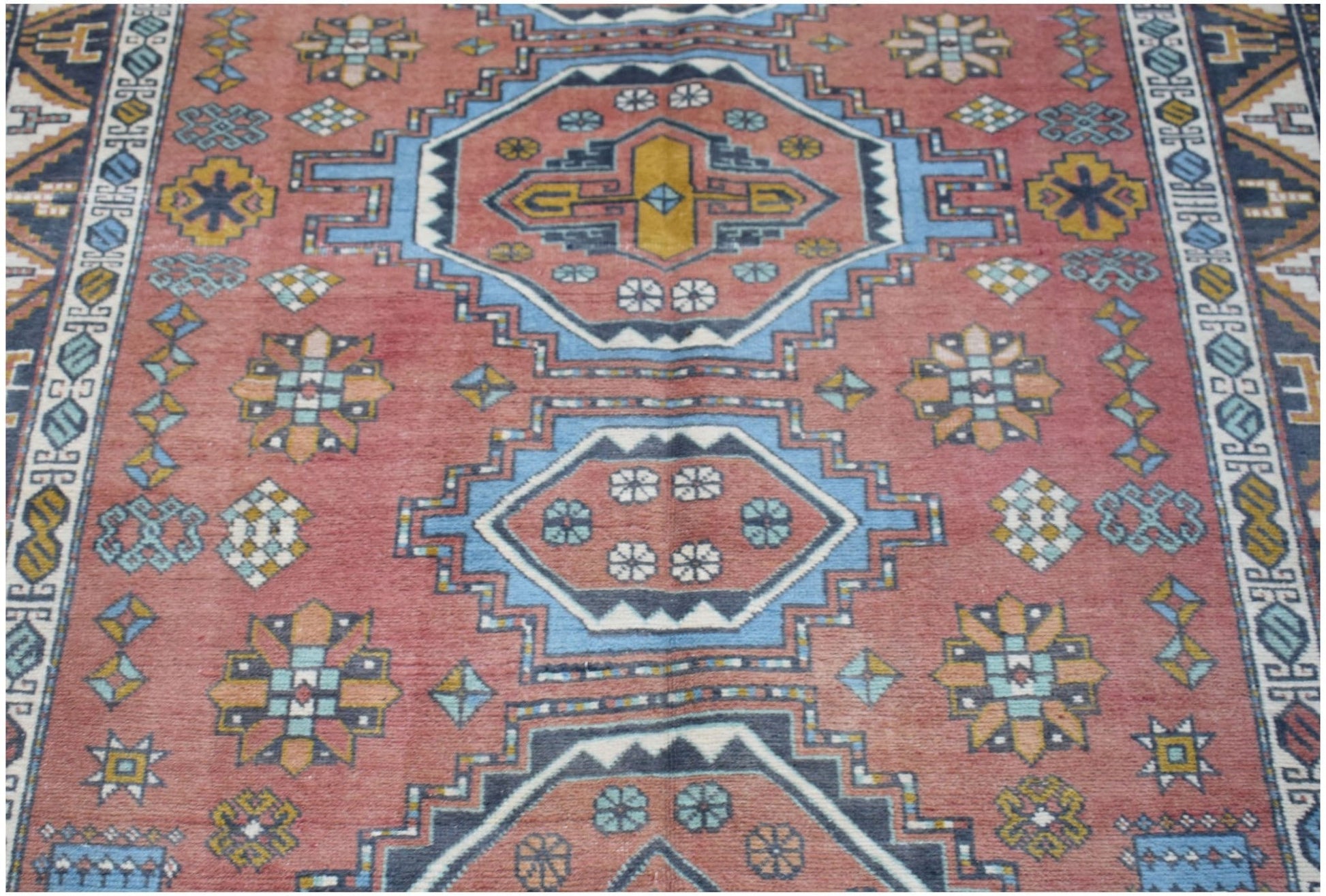 A vintage handwoven Turkish wool rug featuring geometric medallions in red, blue, and yellow.