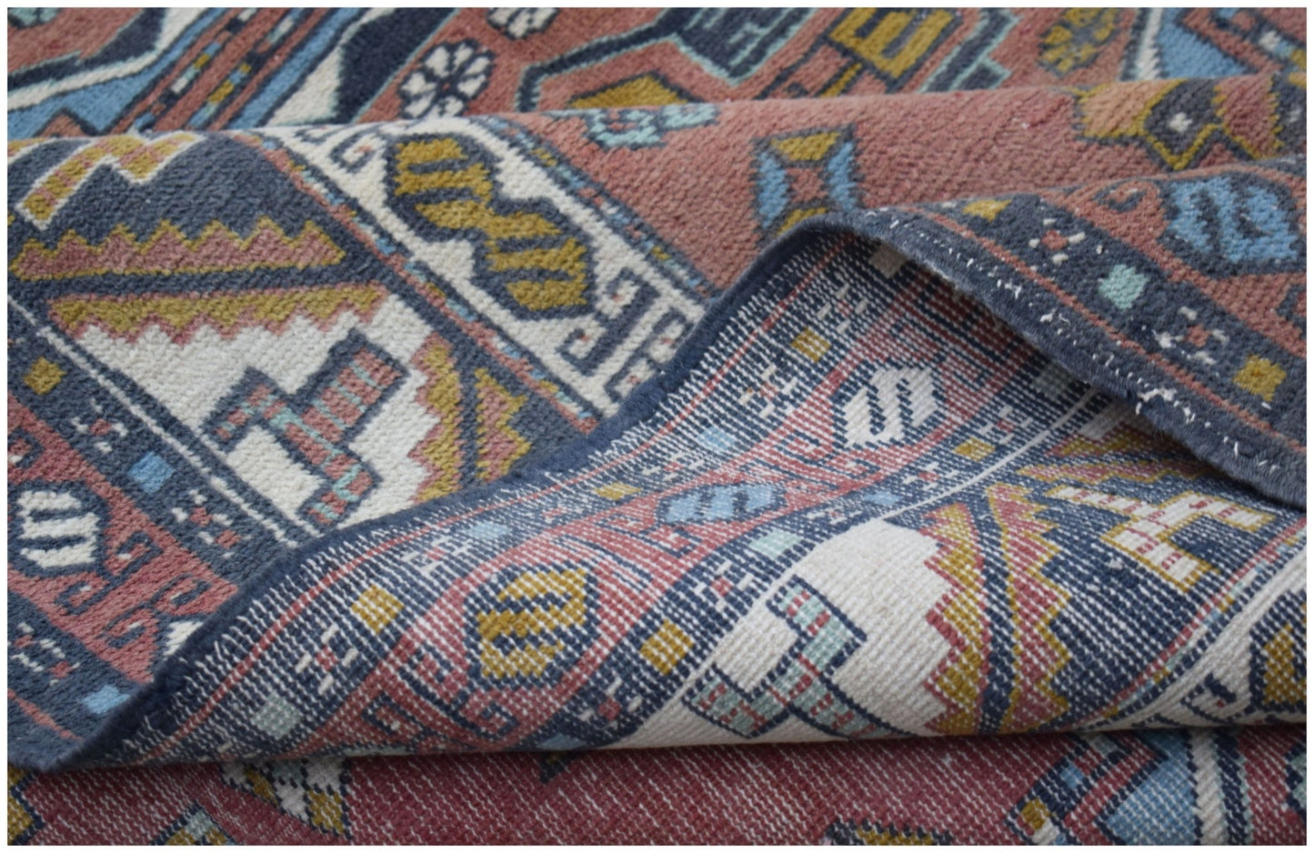 A handwoven vintage Turkish wool rug featuring a geometric pattern in muted red, blue, and yellow.