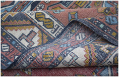 A handwoven vintage Turkish wool rug featuring a geometric pattern in muted red, blue, and yellow.