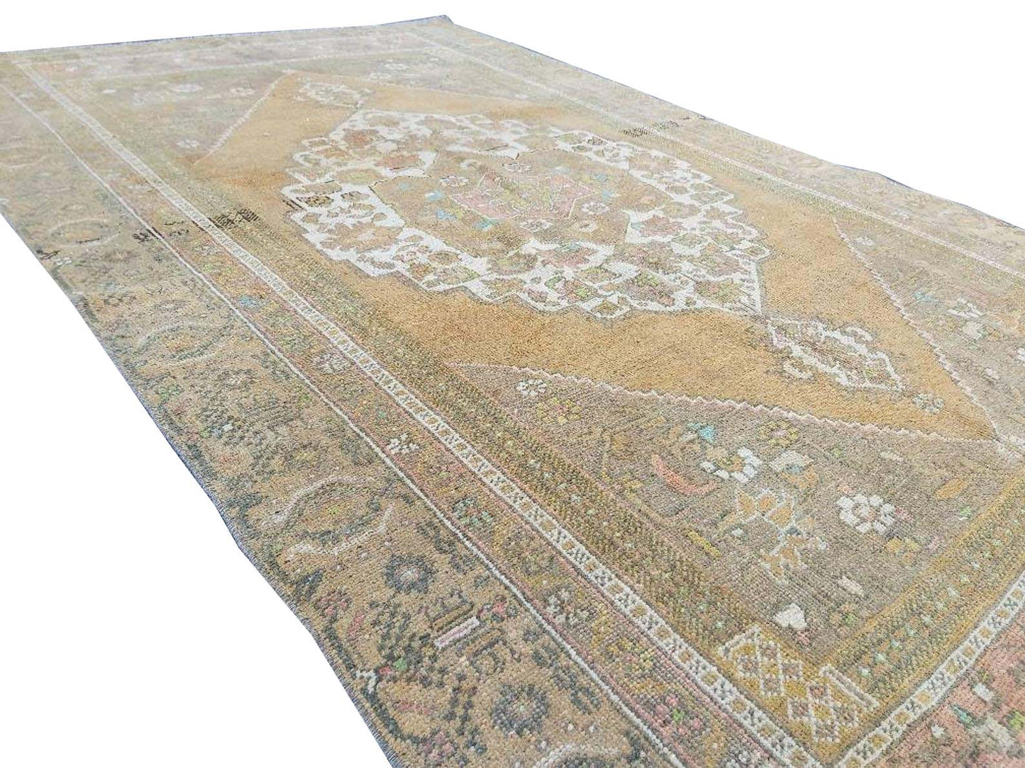 A vintage handmade Turkish wool rug featuring a central medallion on a muted tan background.