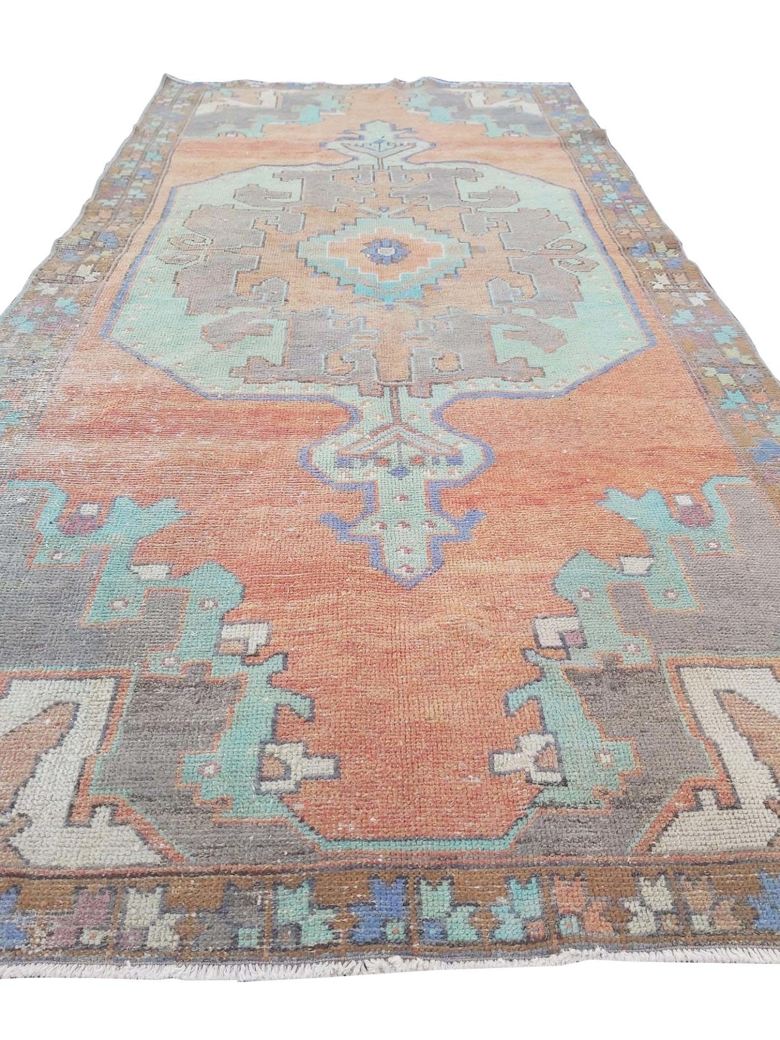 A vintage handmade Turkish rug featuring geometric patterns in orange, teal, and grey.