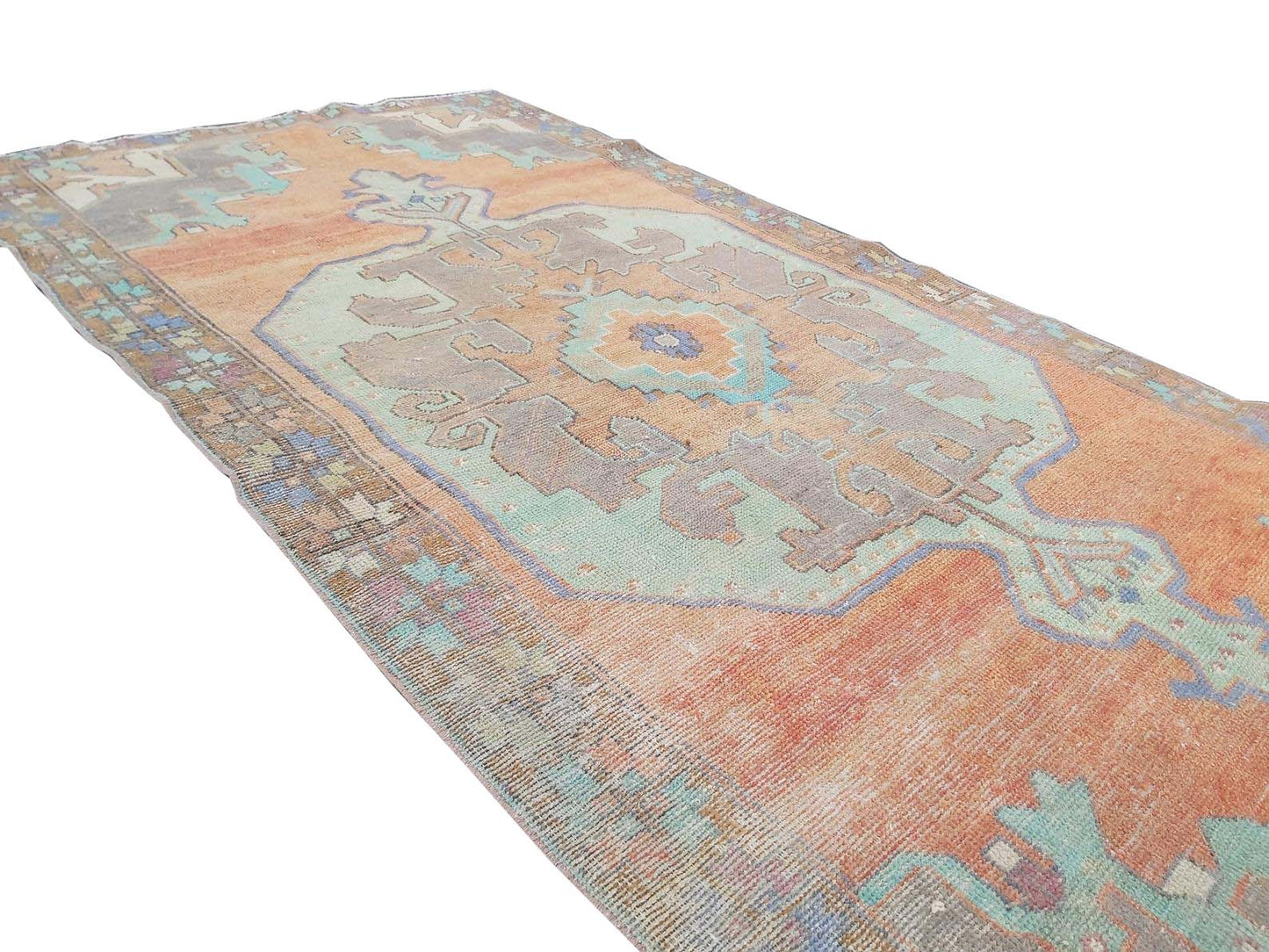 A vintage handmade Turkish rug featuring a geometric medallion in orange and teal tones.
