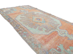 A vintage handmade Turkish rug featuring a geometric medallion in orange and teal tones.