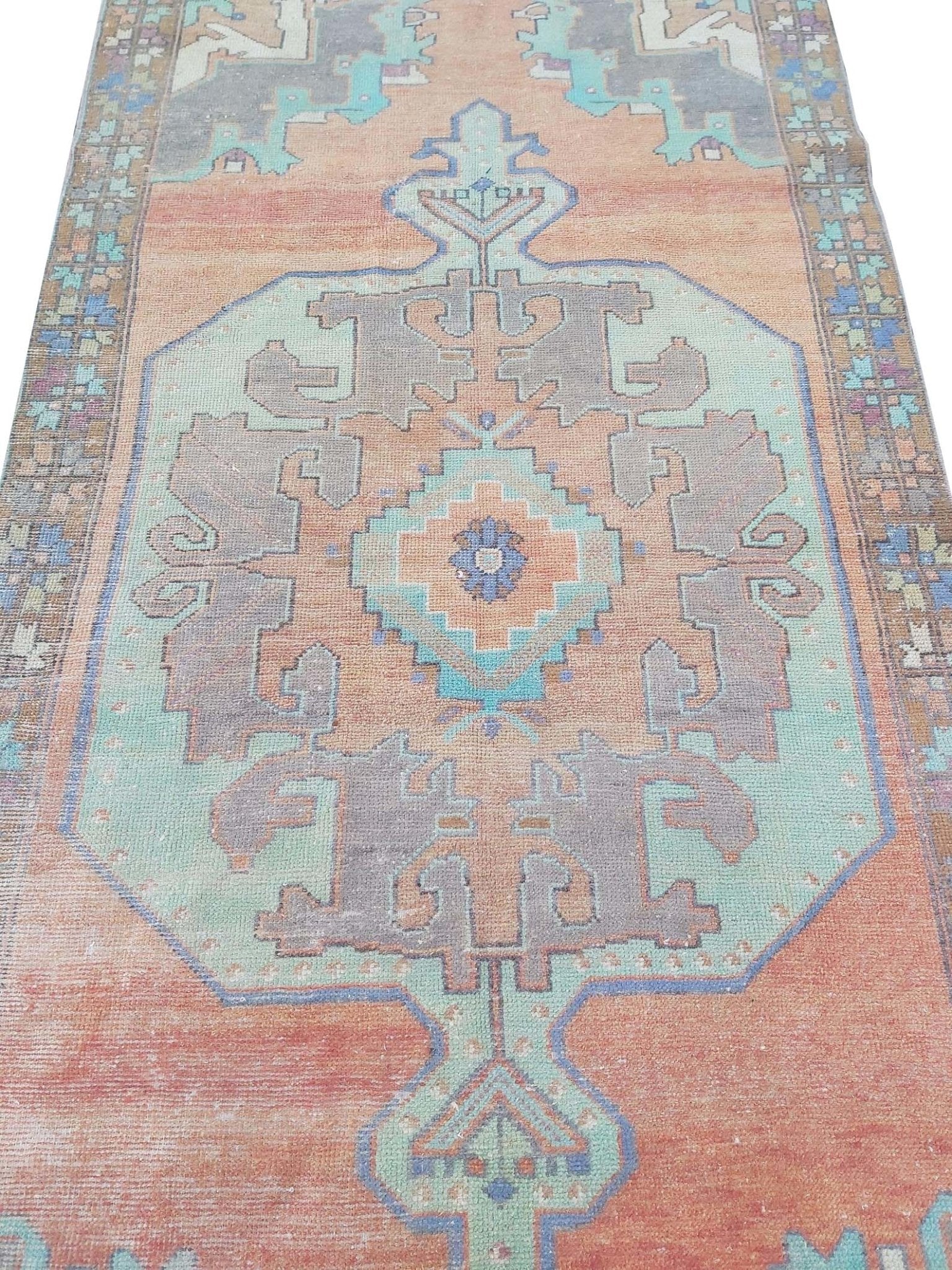 A vintage handmade Turkish rug featuring a geometric medallion in shades of orange and teal.