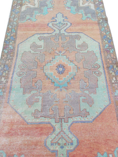 A vintage handmade Turkish rug featuring a geometric medallion in shades of orange and teal.