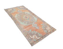 A vintage handmade Turkish rug featuring geometric patterns in orange and teal tones.