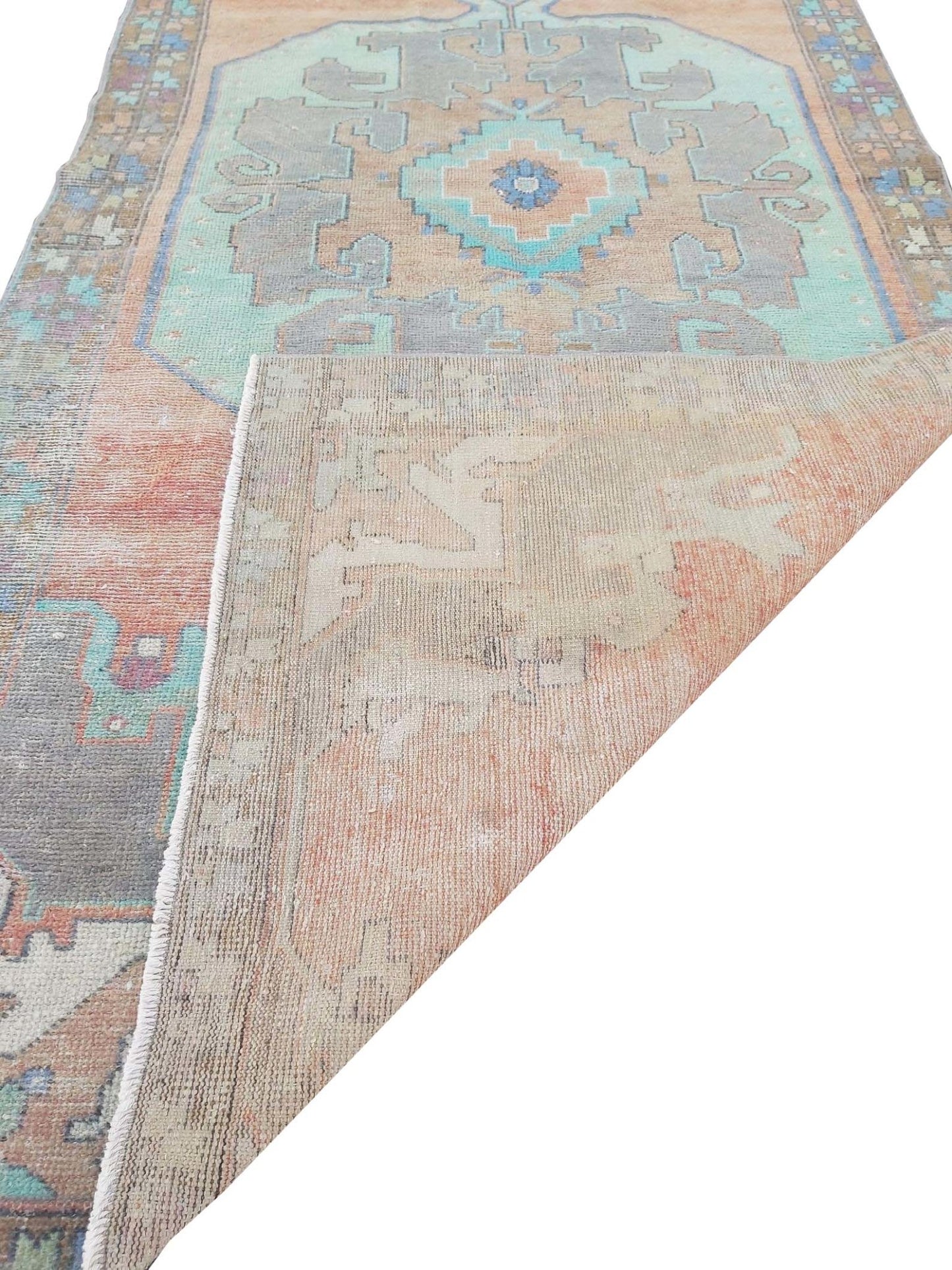 A vintage handmade Turkish wool rug featuring geometric patterns in orange, teal, and grey.
