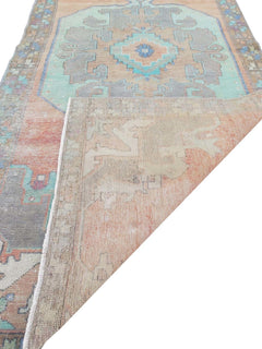 A vintage handmade Turkish wool rug featuring geometric patterns in orange, teal, and grey.