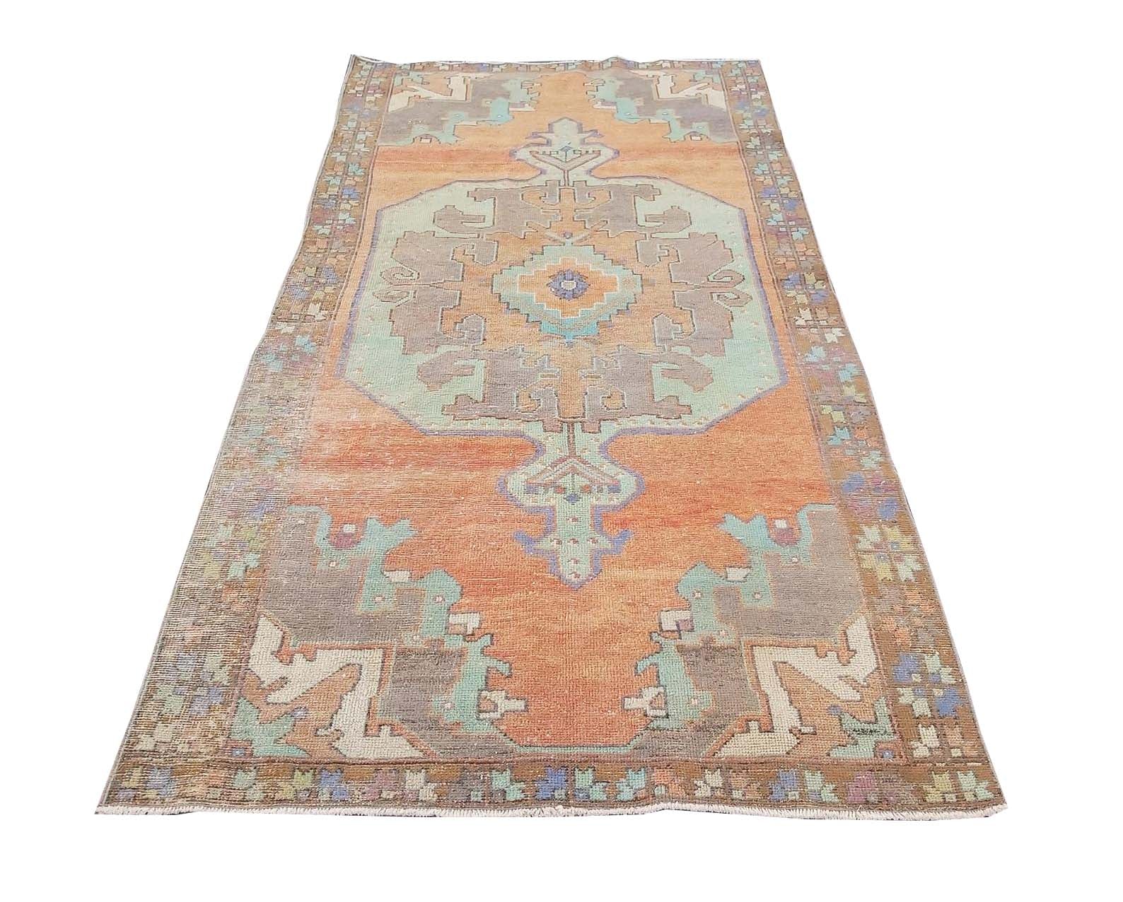 A vintage handmade Turkish rug featuring a geometric medallion in orange, teal, and grey tones.