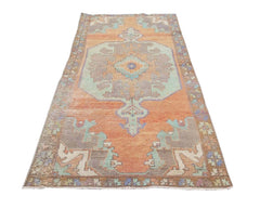 A vintage handmade Turkish rug featuring a geometric medallion in orange, teal, and grey tones.