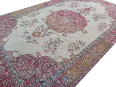 A vintage handmade Turkish wool rug featuring a central medallion and floral motifs in pink and tan.