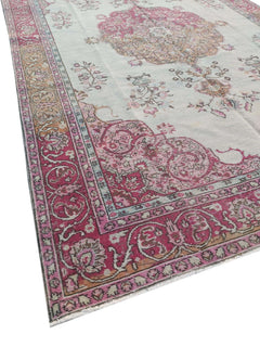 A vintage handmade Turkish wool rug featuring a pink floral medallion on a light cream background.
