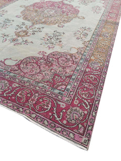 A vintage handmade Turkish wool rug featuring a pink floral medallion on a light cream background.