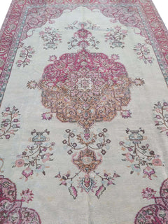 A vintage handmade Turkish wool rug featuring a central medallion and floral motifs in pink tones.