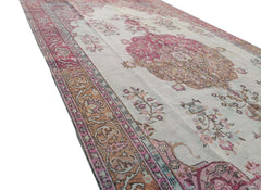 A vintage handmade Turkish wool rug featuring a central medallion and floral motifs in pink and tan.