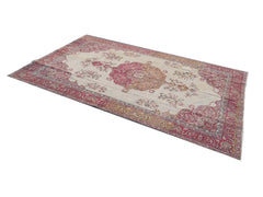 A rectangular vintage Turkish rug featuring a central floral medallion in shades of pink and cream.