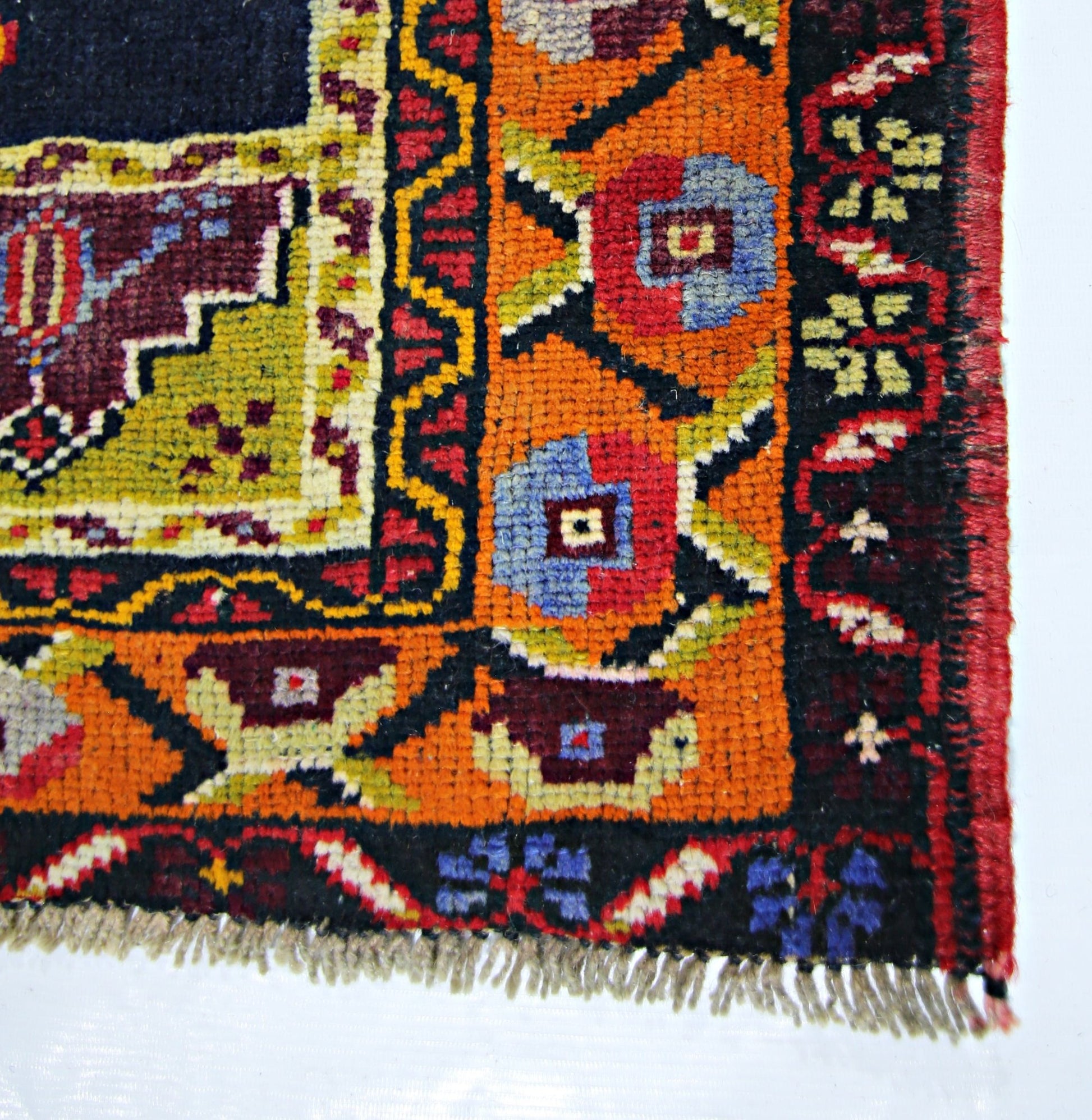 A corner view of a vintage handmade Turkish Taspinar rug featuring geometric floral patterns in orange, red, and blue.