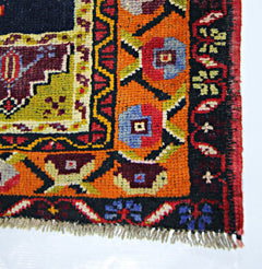 A corner view of a vintage handmade Turkish Taspinar rug featuring geometric floral patterns in orange, red, and blue.