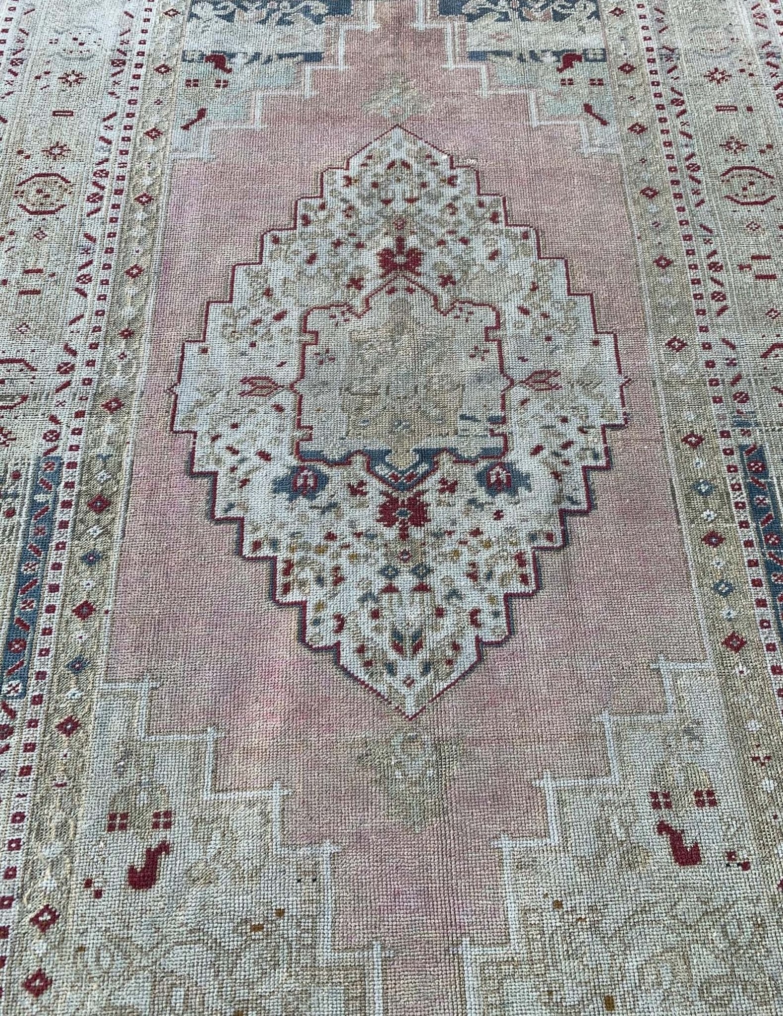 A vintage Turkish Taspinar rug featuring a geometric central medallion in soft pink and beige tones.