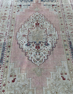 A vintage Turkish Taspinar rug featuring a geometric central medallion in soft pink and beige tones.