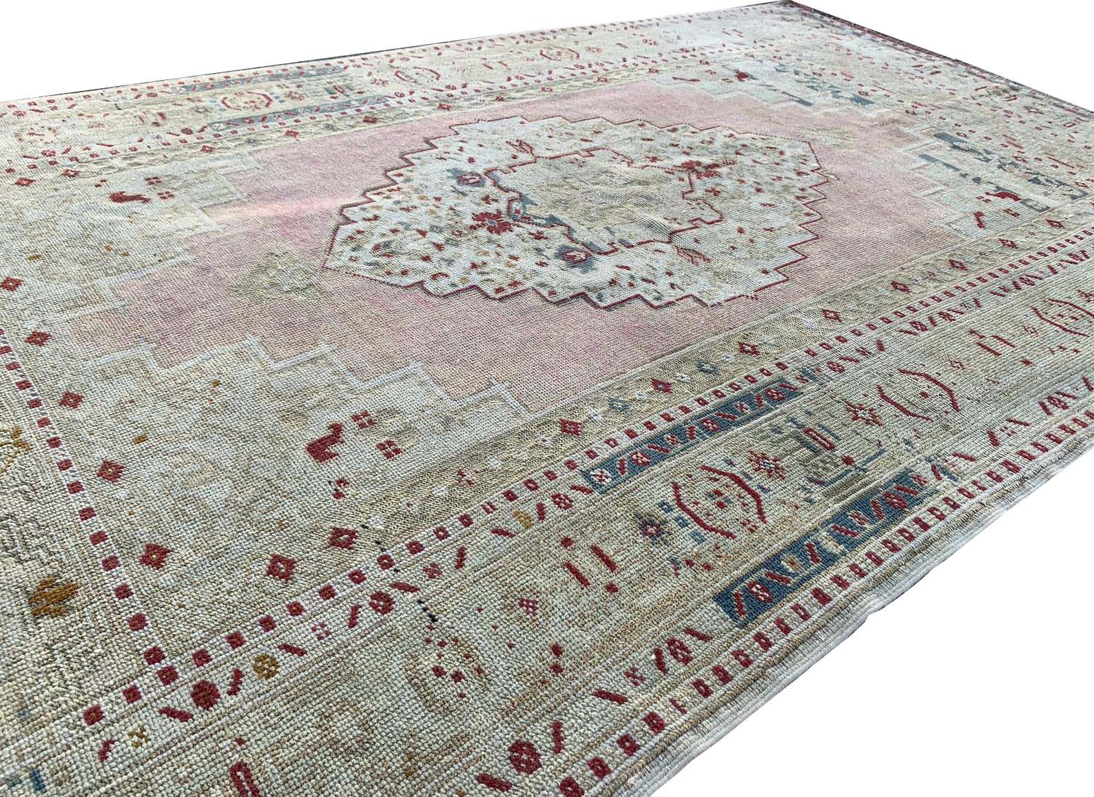 A vintage Turkish Taspinar rug featuring a soft pink field with geometric motifs and a beige border.