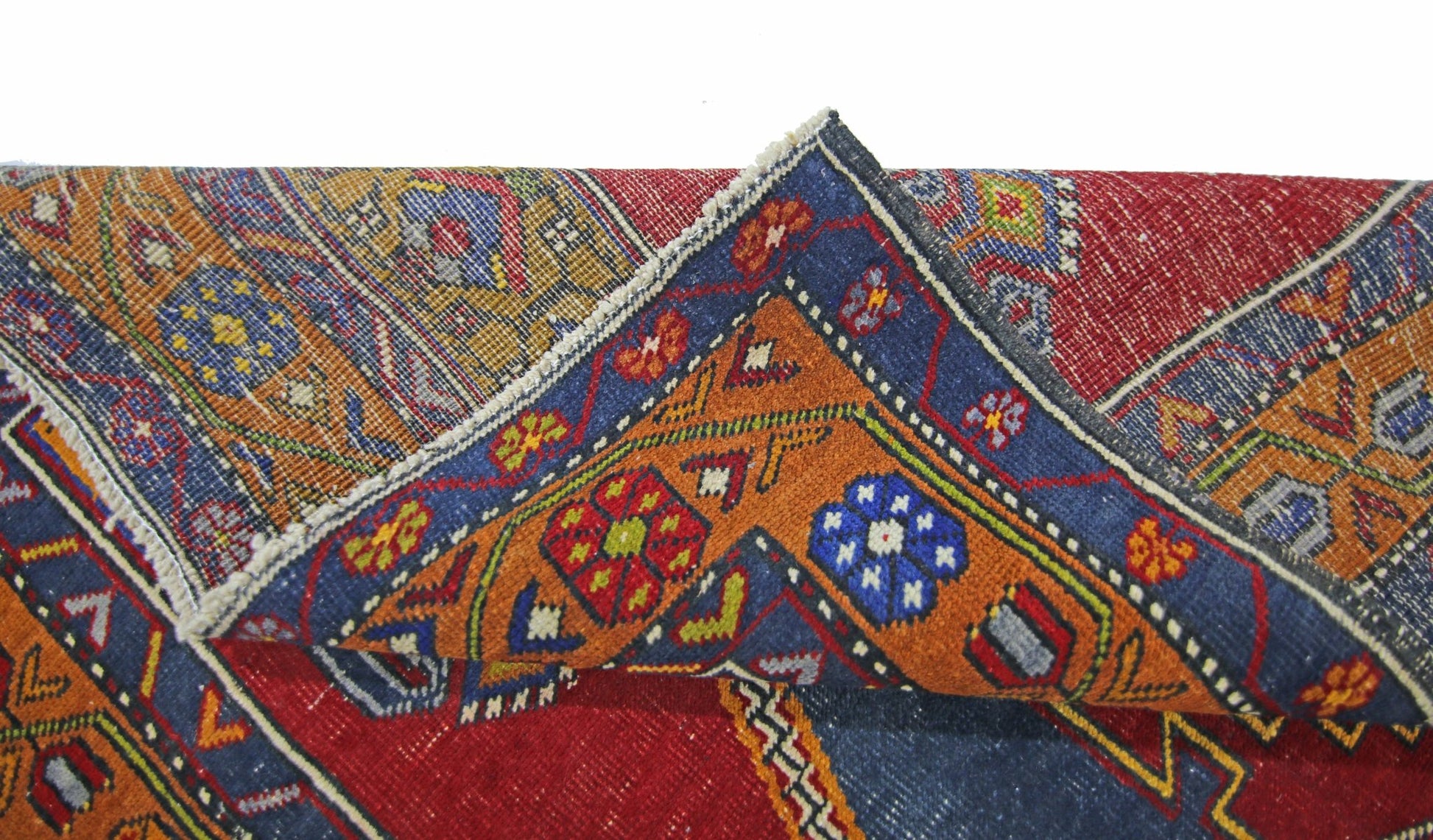 A folded vintage Turkish Taspinar rug featuring intricate geometric patterns in red, blue, and orange.