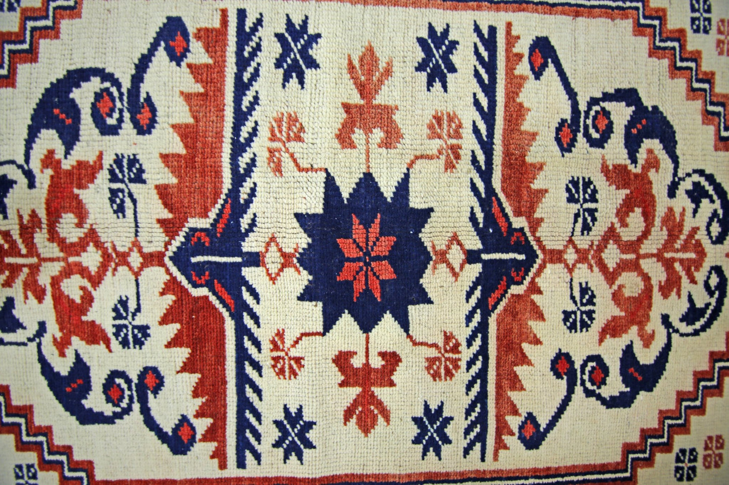 A vintage handmade Turkish rug featuring a central blue star motif with red floral accents on a cream background.