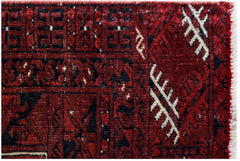 A close-up of a vintage Afghan Turkmen rug featuring geometric patterns in red, blue, and ivory.