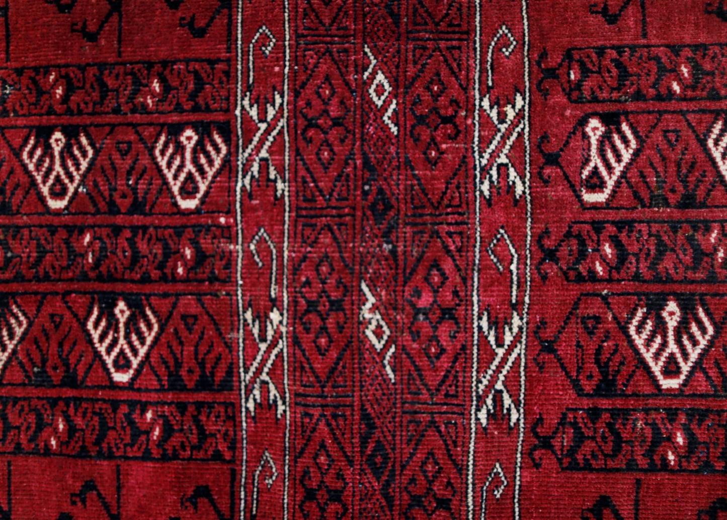 A vintage Afghan Turkmen rug featuring intricate geometric patterns in deep red, black, and ivory.