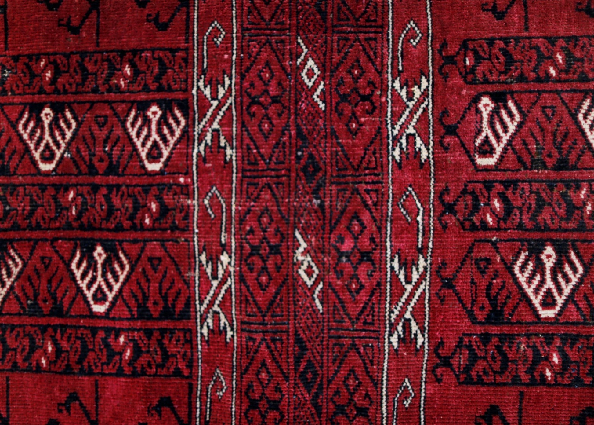 A vintage Afghan Turkmen rug featuring intricate geometric patterns in deep red, black, and ivory.
