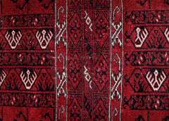 A vintage Afghan Turkmen rug featuring intricate geometric patterns in deep red, black, and ivory.