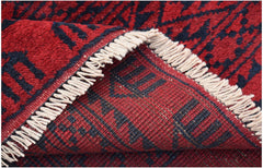 A close-up of a handmade Afghan Turkmen rug featuring a red and black geometric elephant foot motif.