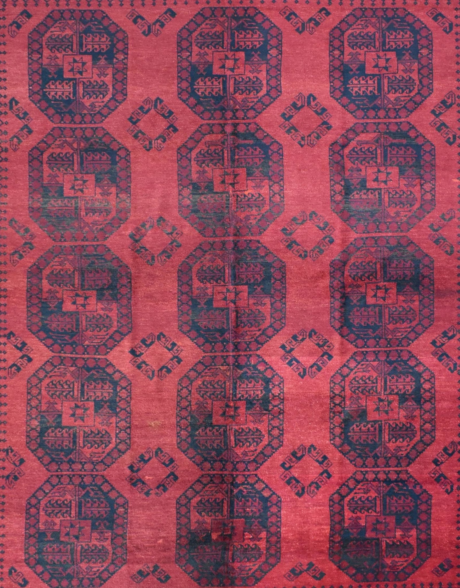 A vintage Afghan Turkmen rug featuring a repeating geometric pattern in deep red and dark blue.