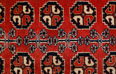 A vintage Afghan Baluch rug featuring a repeating geometric pattern in red, black, and cream.