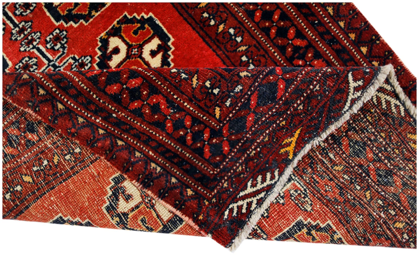 A vintage handmade Afghan Baluch rug with a folded corner revealing its red and dark blue pattern.