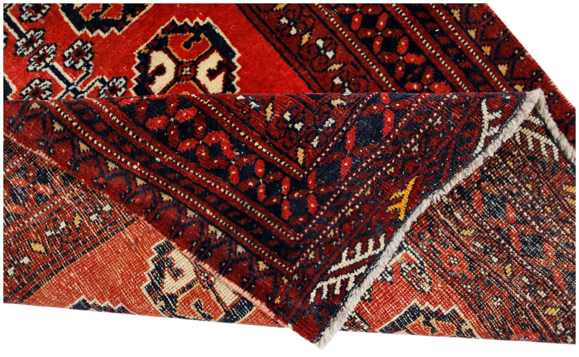 A vintage handmade Afghan Baluch rug with a folded corner revealing its red and dark blue pattern.