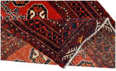 A vintage handmade Afghan Baluch rug with a folded corner revealing its red and dark blue pattern.