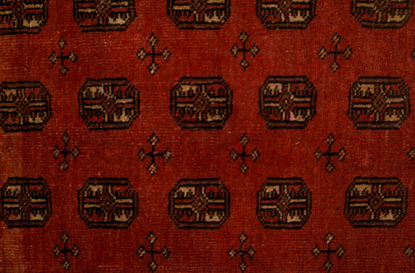 A vintage handwoven Afghan rug featuring a repeating geometric pattern on a deep red background.